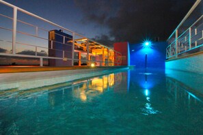 Un espace piscine nocturne offrant une vue dégagée sur le bord de la piscine, éclairé d’une lumière bleue, et un bâtiment doté d’une façade en verre.