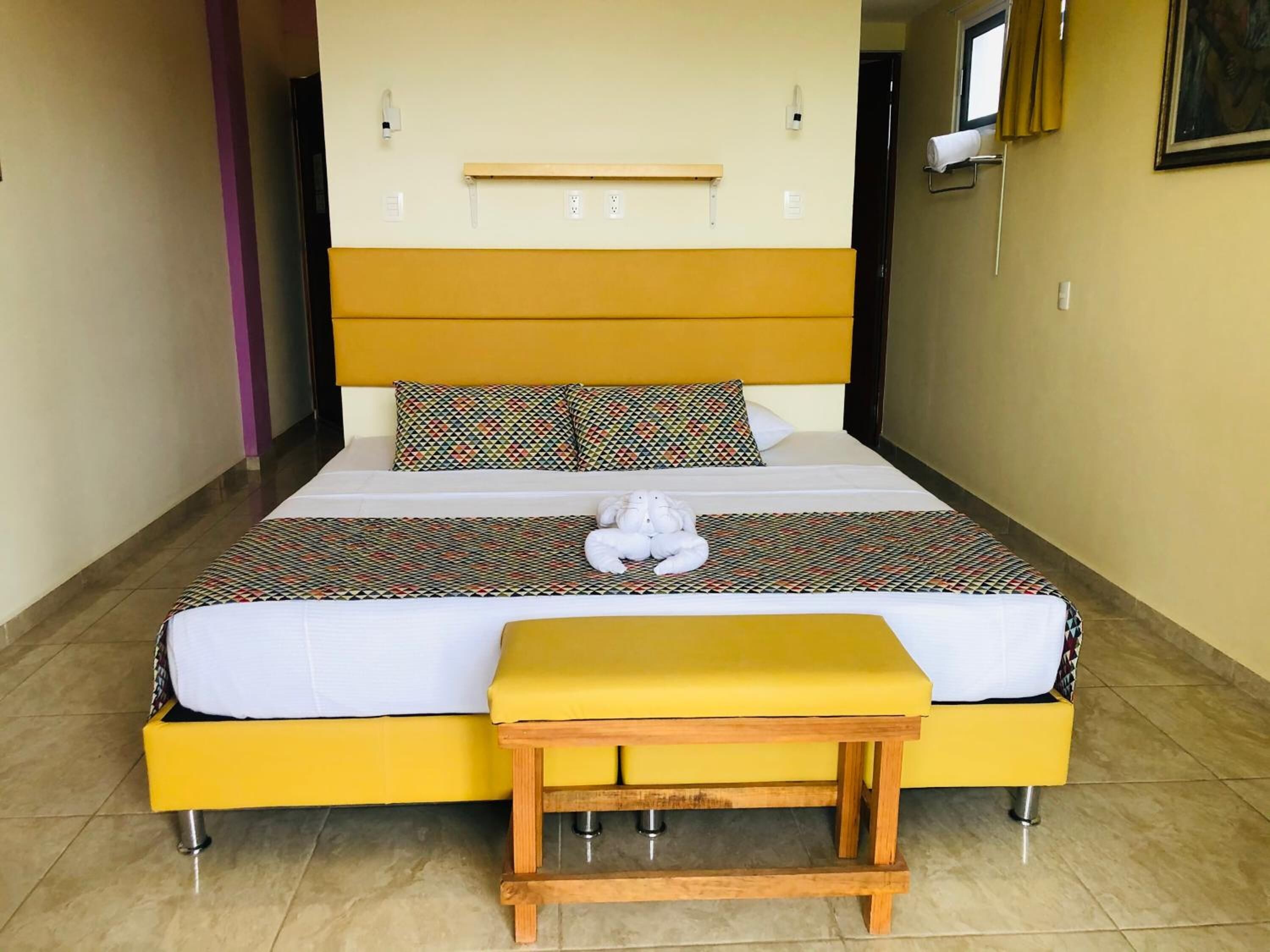 A bed with a yellow headboard, patterned pillows, and a bedside table with a yellow cushion.