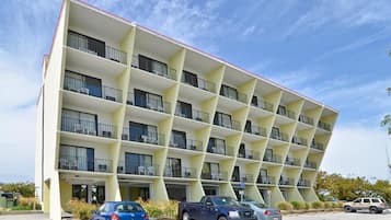A multi-story hotel with a unique angular facade, balconies on each floor, and a parking lot with several cars.