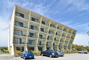 A multi-story hotel with a unique angular facade, balconies on each floor, and a parking lot with several cars. - Sea Bay Hotel (Ocean City)