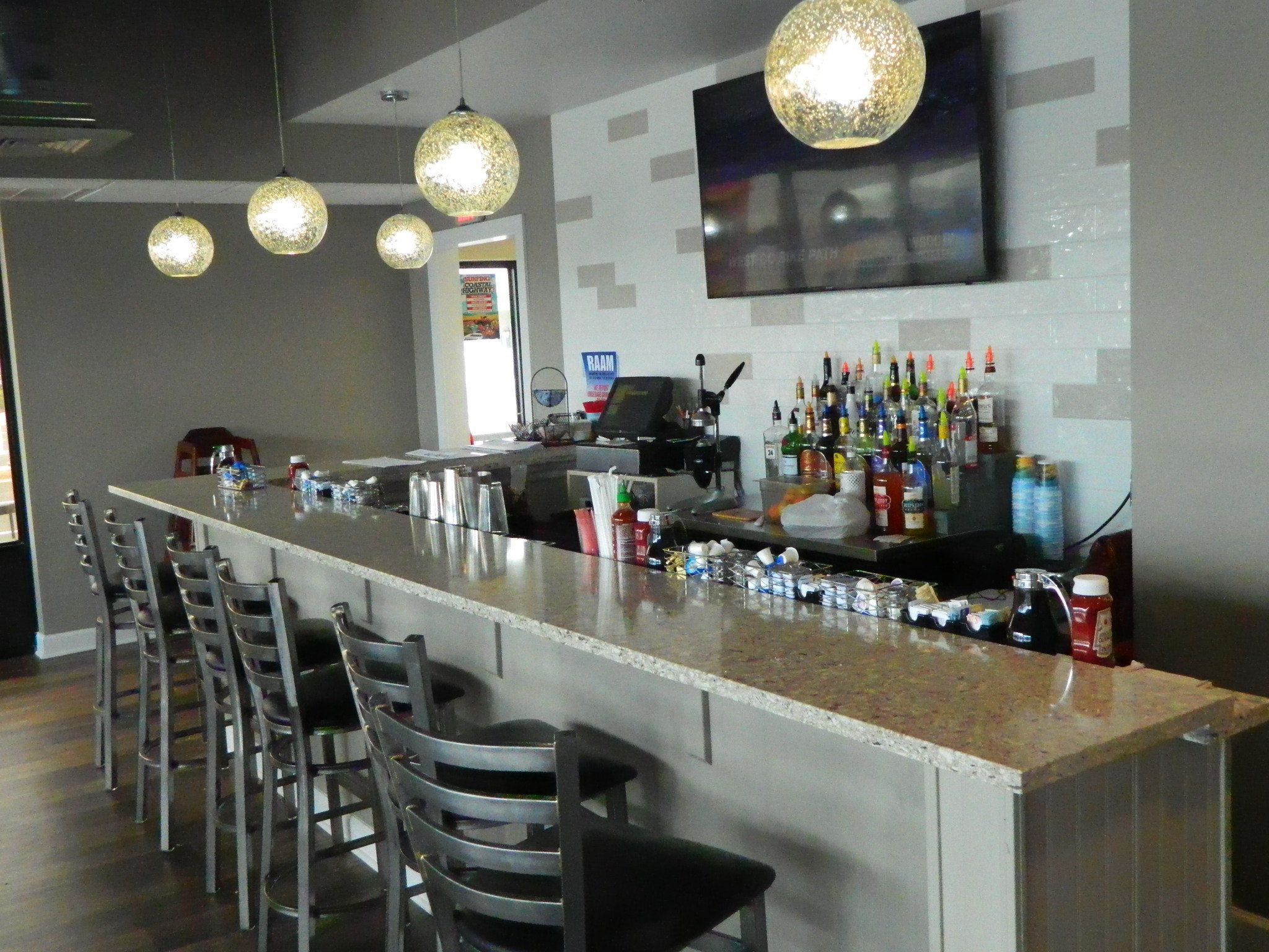 A bar area with a long counter, multiple chairs, hanging pendant lights, and a television mounted on the wall.
