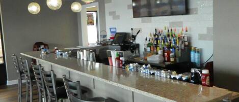 A bar area with a long counter, multiple chairs, hanging pendant lights, and a television mounted on the wall.