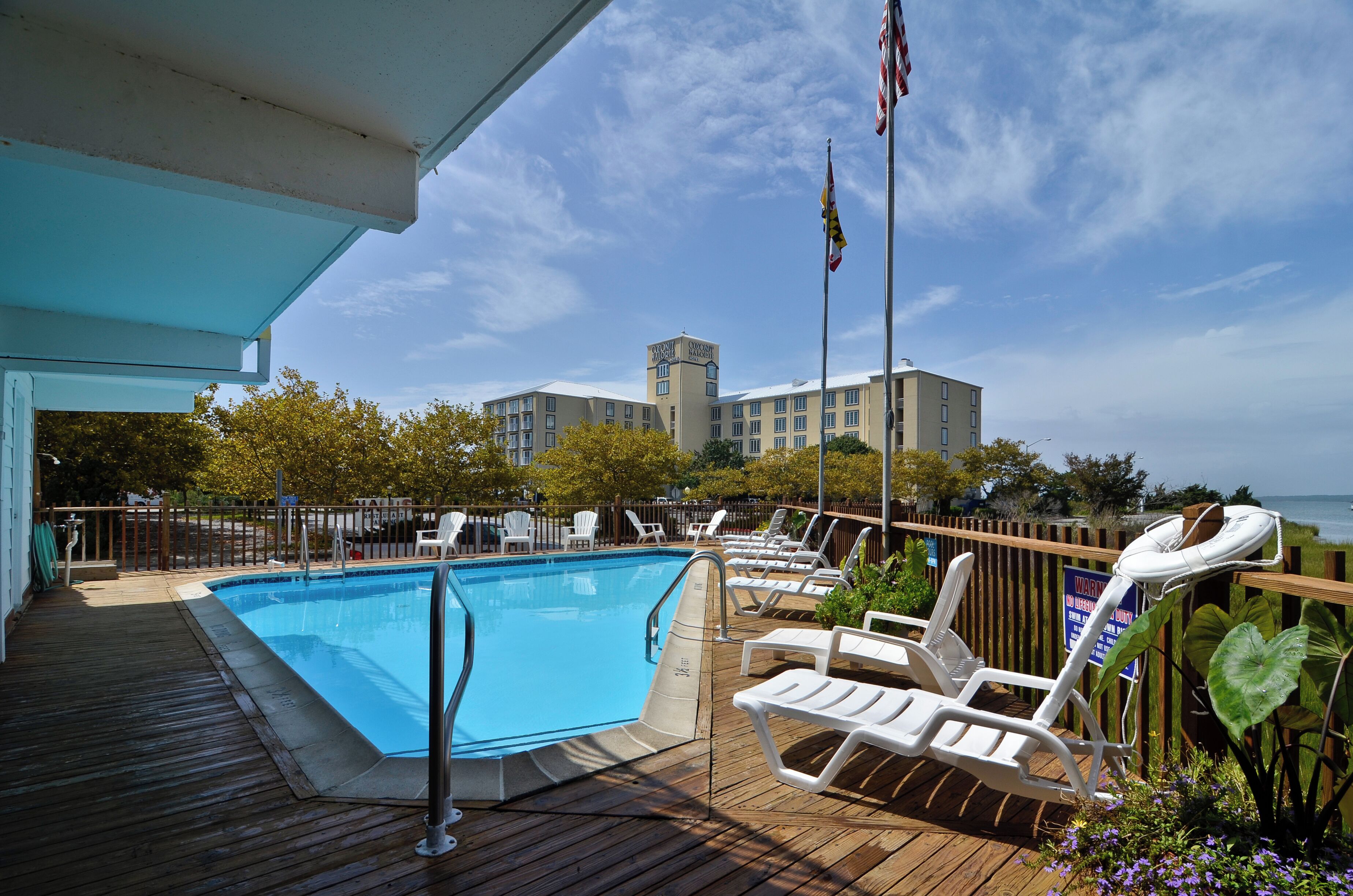 A poolside area with lounge chairs, a pool, and a view of a building in the background.