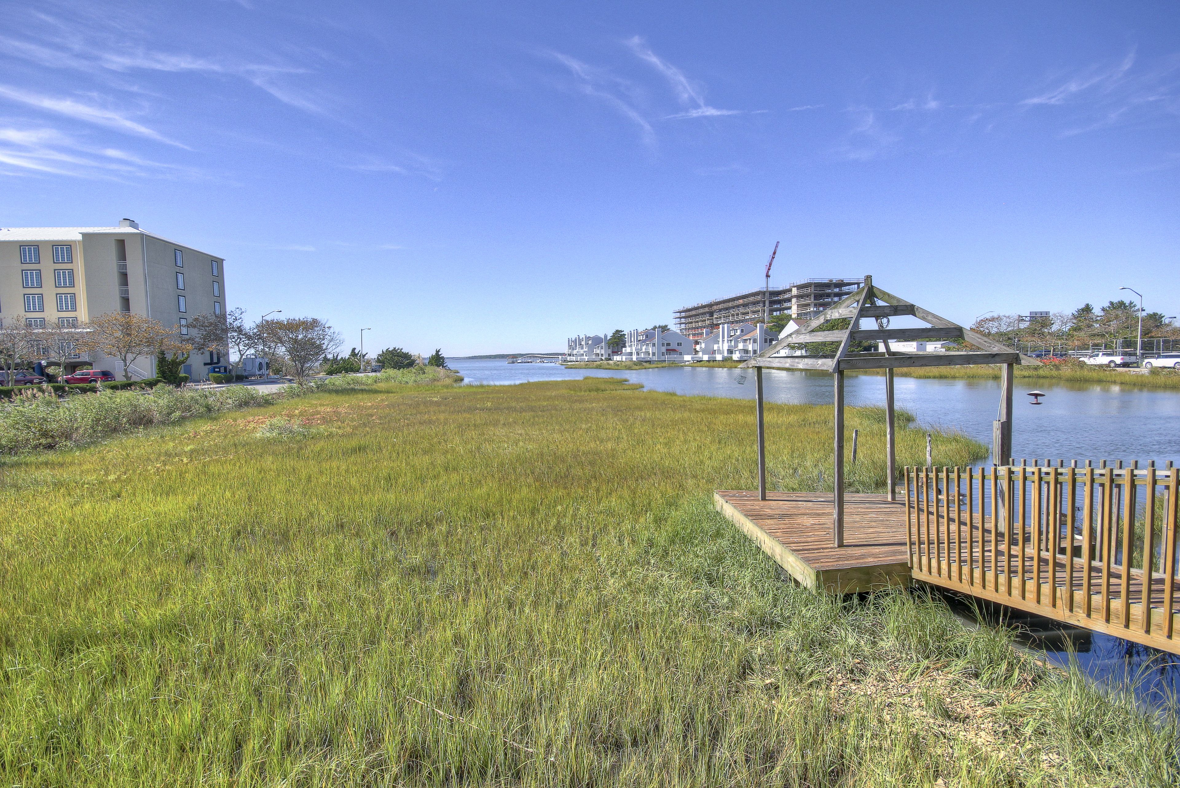 A riverside park with a wooden gazebo, a grassy field, and a building in the background.