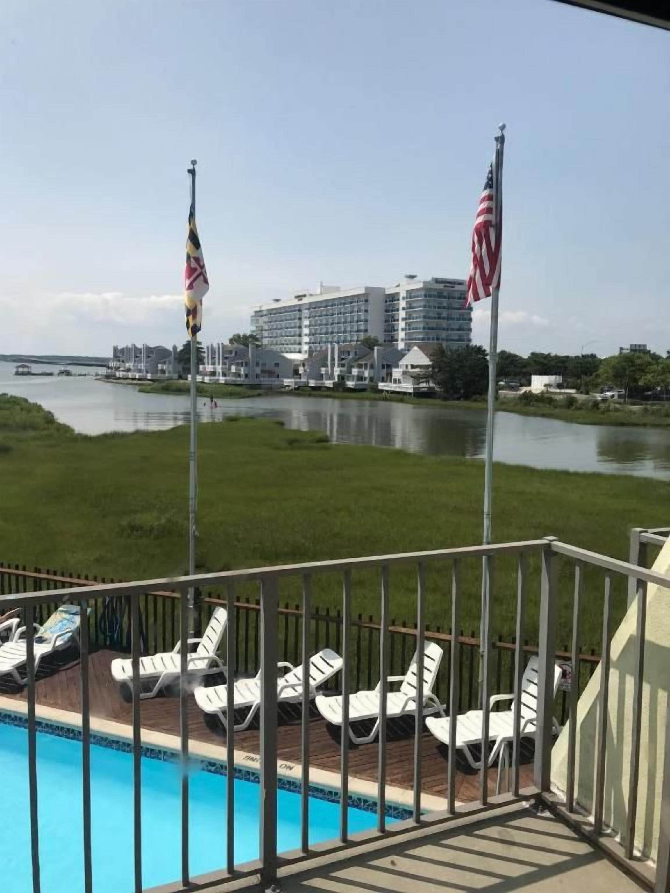 A pool area with lounge chairs, a flagpole with an American flag, and a building in the background.