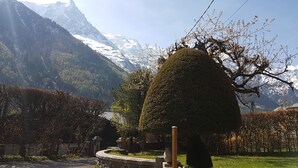 Un paysage montagneux aux sommets enneigés, un jardin bien entretenu avec des haies taillées avec soin et un sentier en pierre.