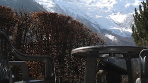 Une vue sur une chaîne de montagnes dont les sommets sont couverts de neige, un ciel bleu dégagé et un espace aménagé avec des chaises en plastique et une table.