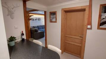 A hallway with a wooden door, a dining area with a table and chairs, a potted plant, and a mounted deer head.