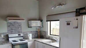 A compact kitchen with white appliances, a microwave, and a refrigerator. - Caths cottage on Mayfair (Whangamata)