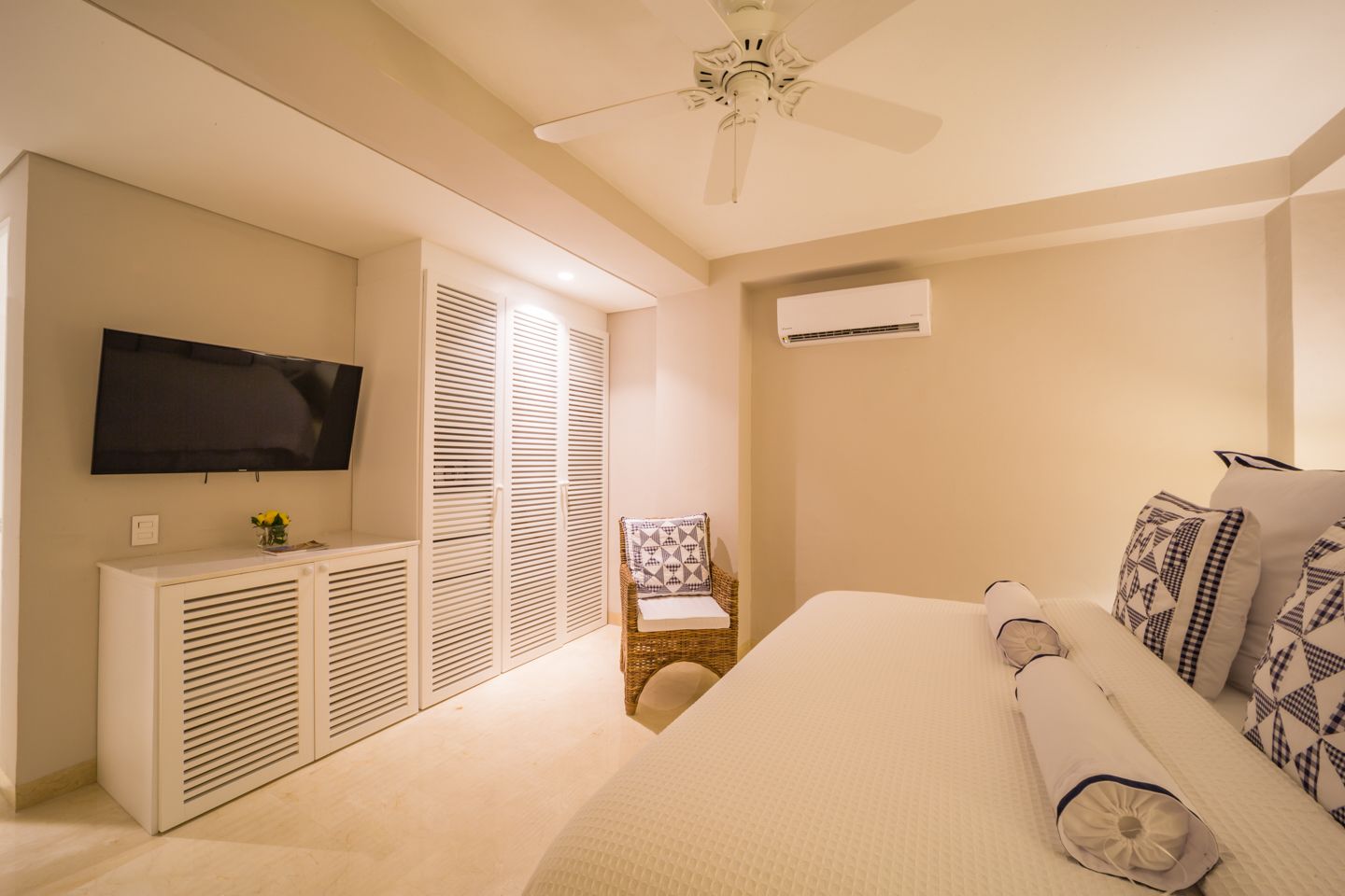 Un dormitorio con cama, televisor, ventilador de techo y aire acondicionado.