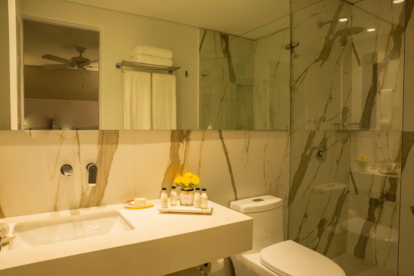 A modern bathroom with a marble vanity, a toilet, and a glass-enclosed shower.