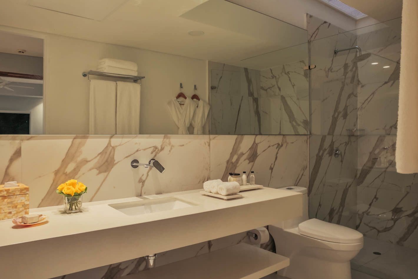 Un baño moderno con tocador de mármol, un espejo grande y una cabina de ducha de vidrio.