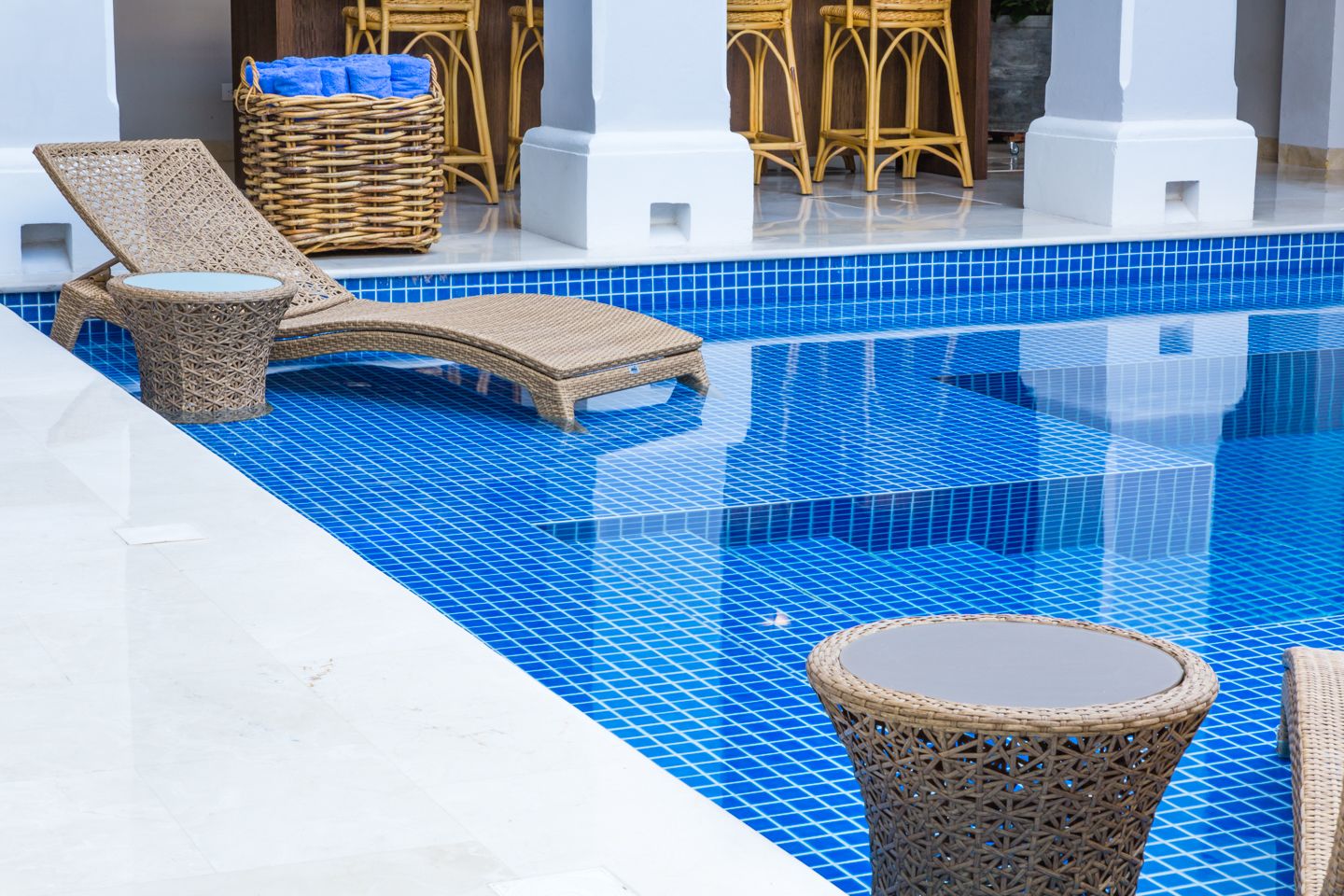 Zona de piscina amb gandules de vimet i una taula rodona.