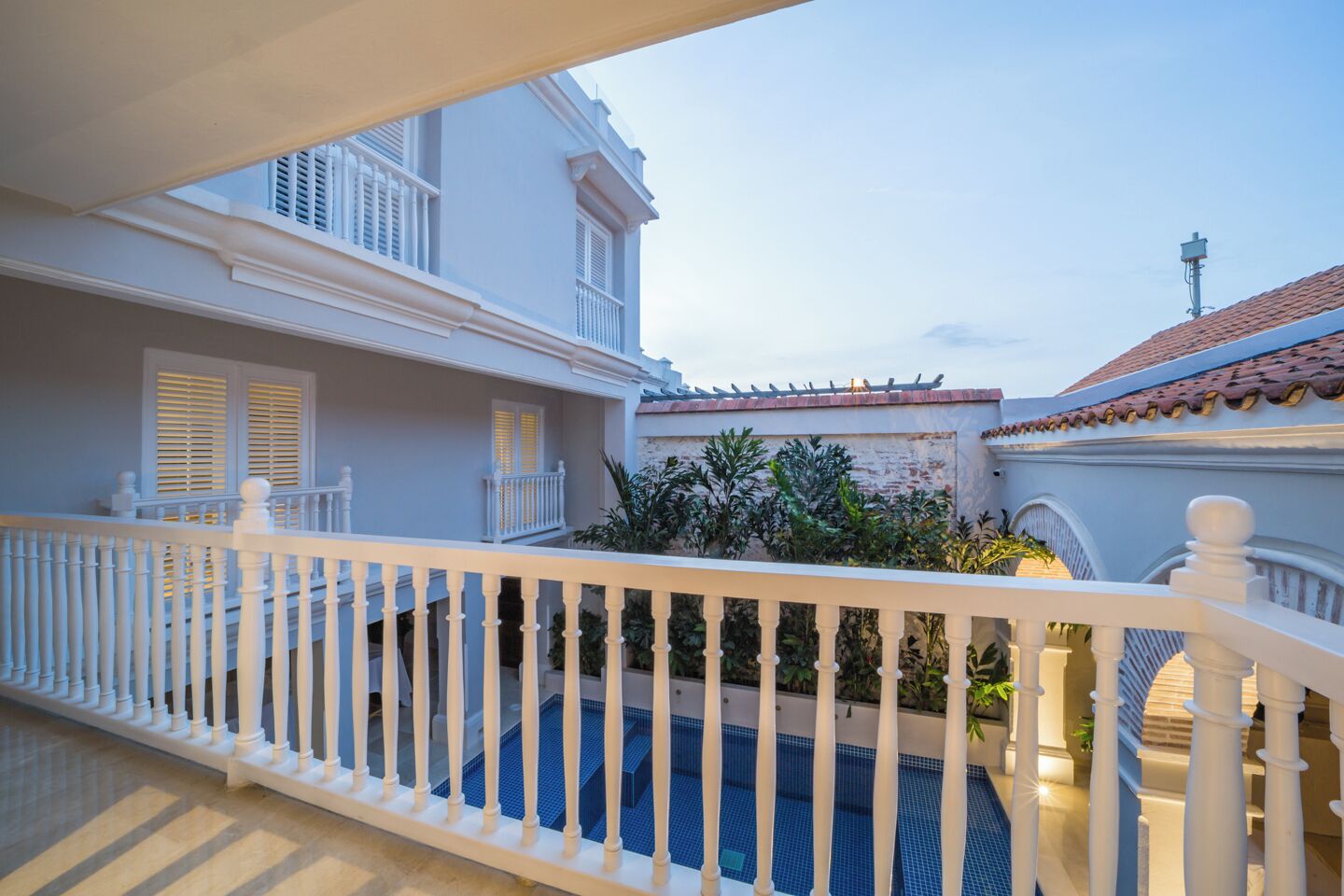 A courtyard with a swimming pool, white railings, and a building with a tiled roof.