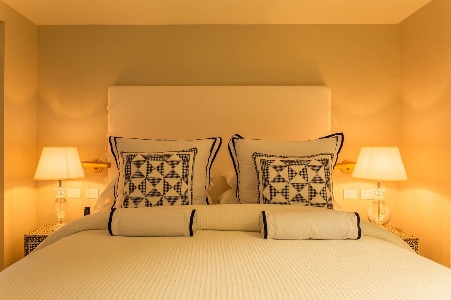 A hotel room with a large bed, two bedside lamps, and a headboard with a geometric pattern.