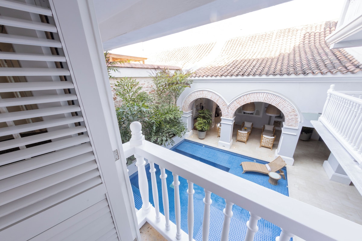 A balcony with a pool, white railings, and a tiled roof in the background.