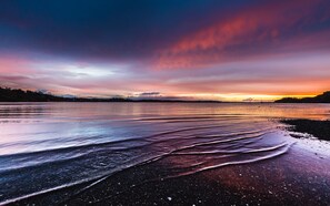 Una playa con olas suaves y un atardecer sobre el agua.