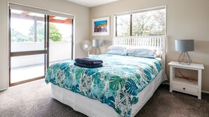 A bedroom with a bed, a nightstand, a fan, and a window with a view of trees. - Relax on Ridge | 7 seater car included (Oneroa)
