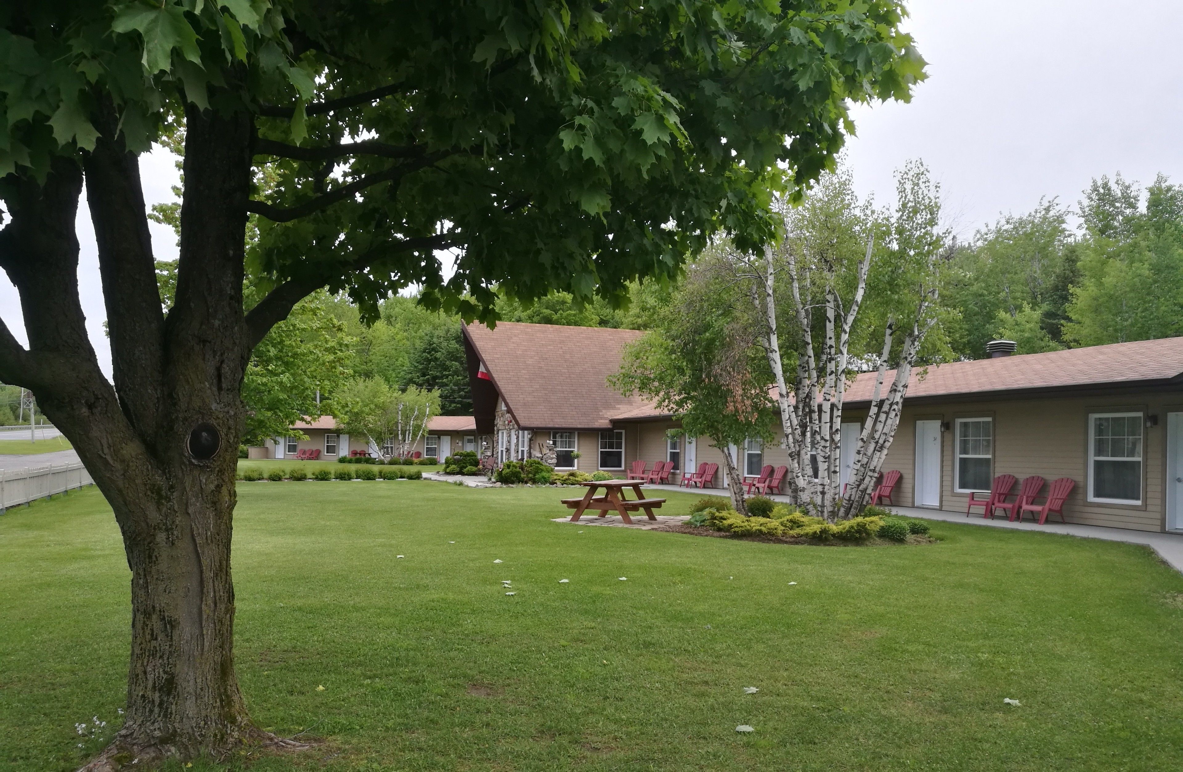 Un motel con césped cuidado, mesa de picnic y sillas rojas.