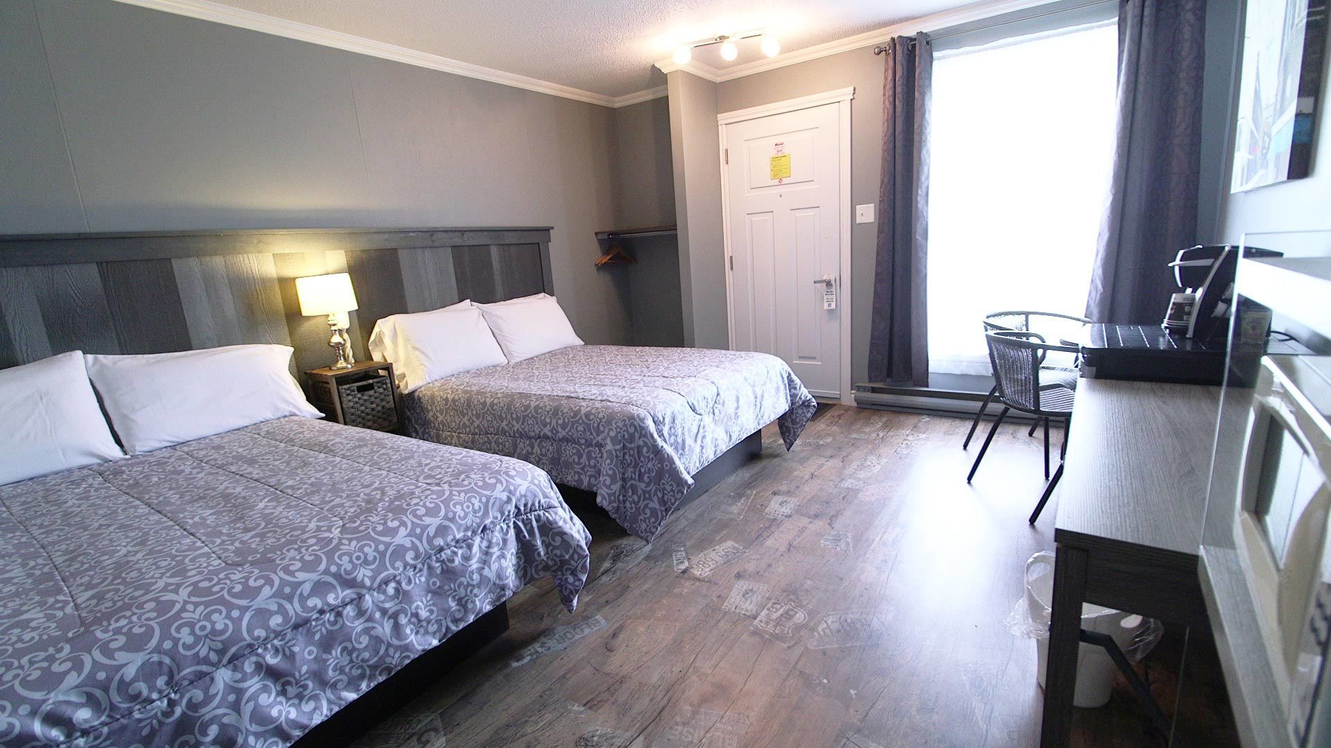 A hotel room with two beds, a desk, a chair, and a window with curtains.
