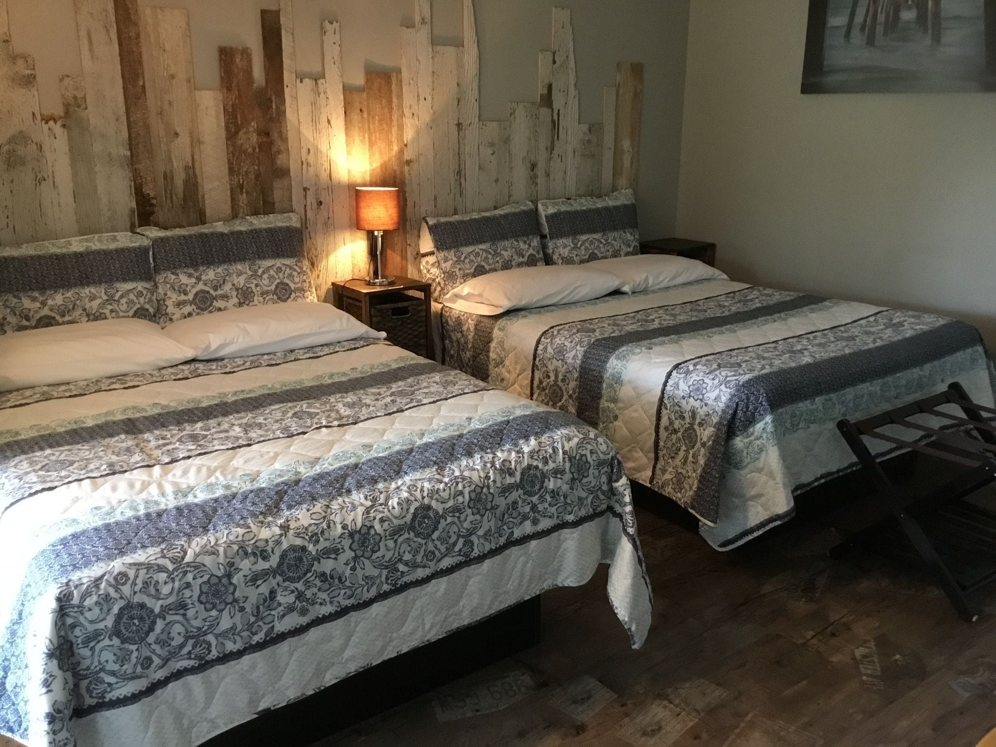 A bedroom with two beds, a nightstand, a lamp, and a wooden headboard.