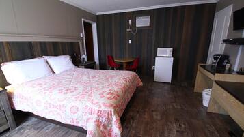 A hotel room with a bed, a small kitchenette, a microwave, a refrigerator, a table with two chairs, and a trash bin.