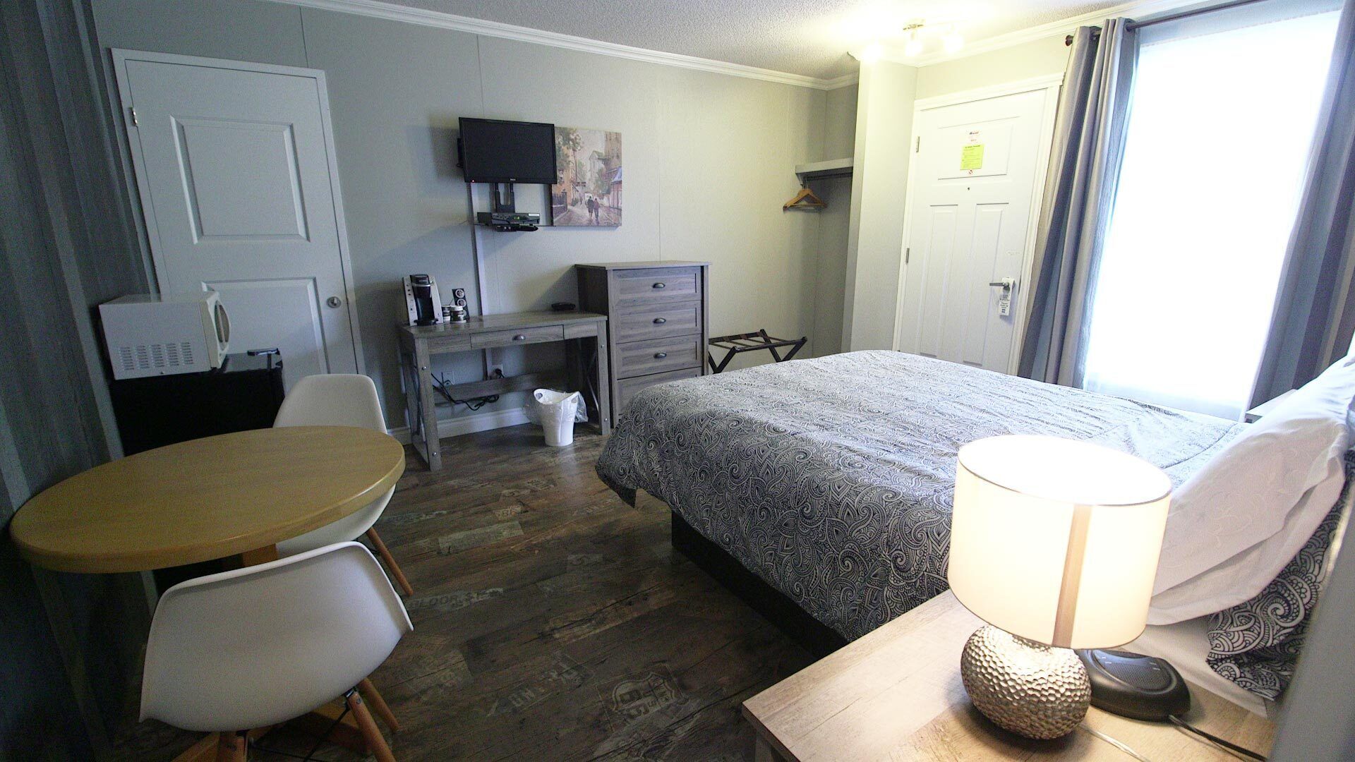 A hotel room with a bed, a desk, a chair, a table, a lamp, and a television.