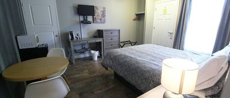 A hotel room with a bed, a desk, a chair, a table, a lamp, and a television.