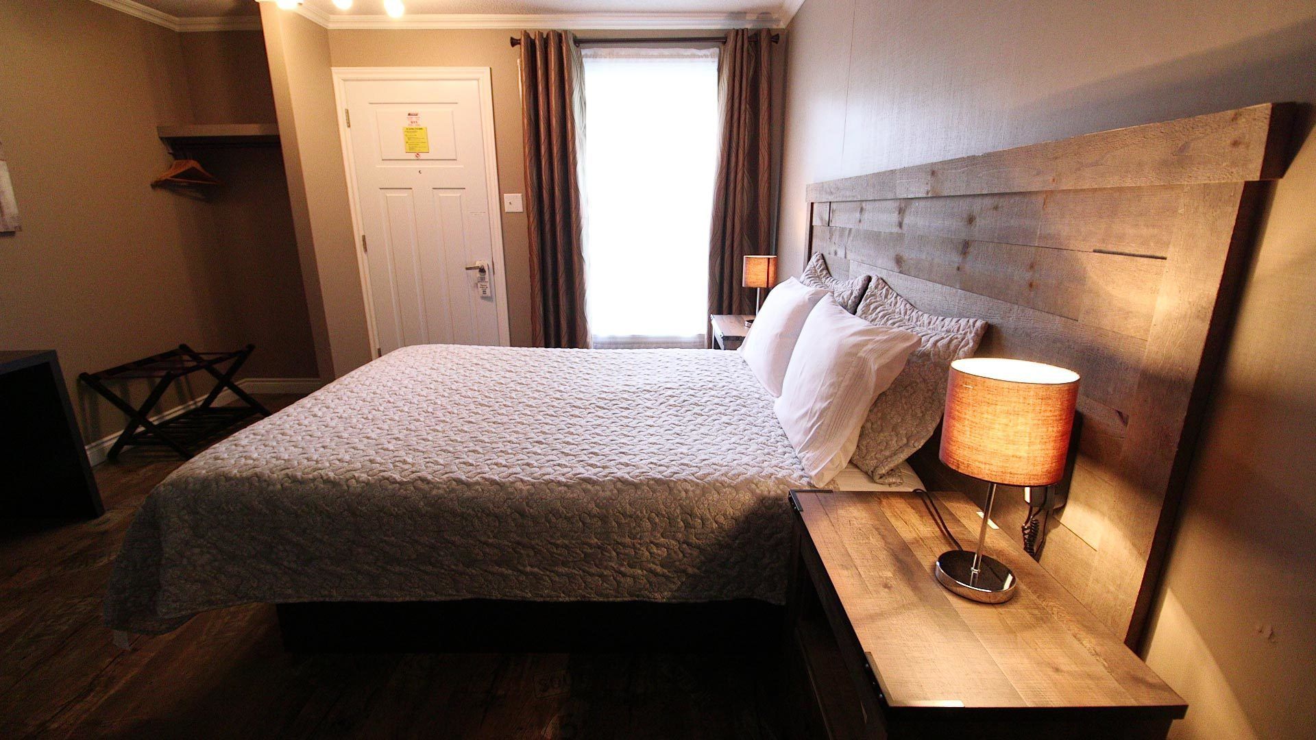 Una cama bien hecha con un edredón texturizado, una lámpara de noche y un cabecero de madera.