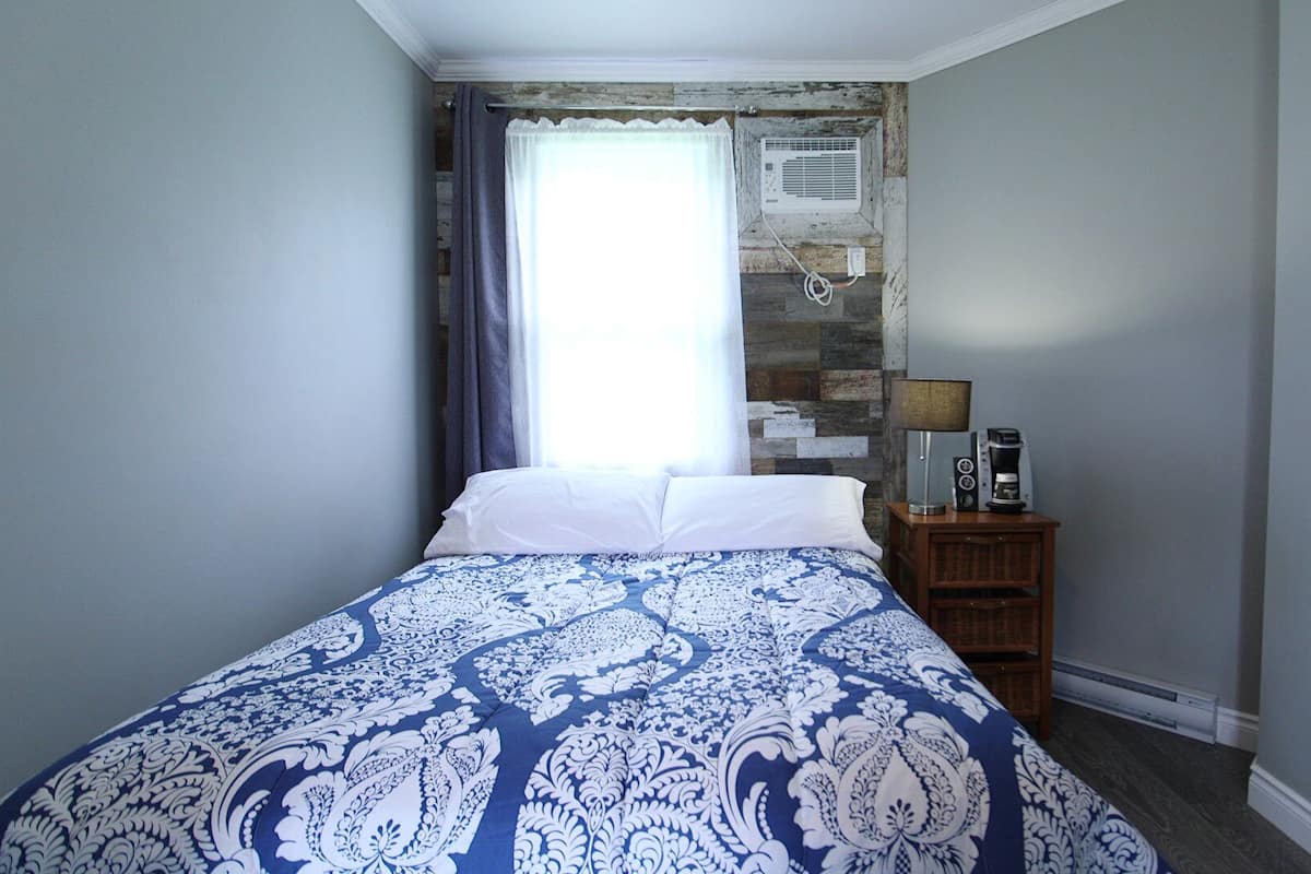 Une chambre à coucher comprenant un lit, une table de chevet avec une lampe, une machine à café et un climatiseur fixé au mur.