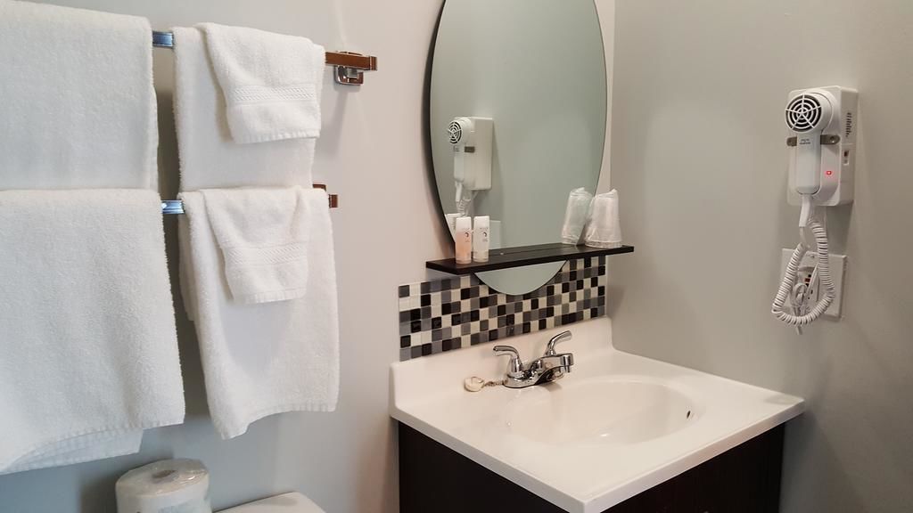 Un baño con lavamanos blanco, espejo, secador de pelo y toallero con toallas blancas.