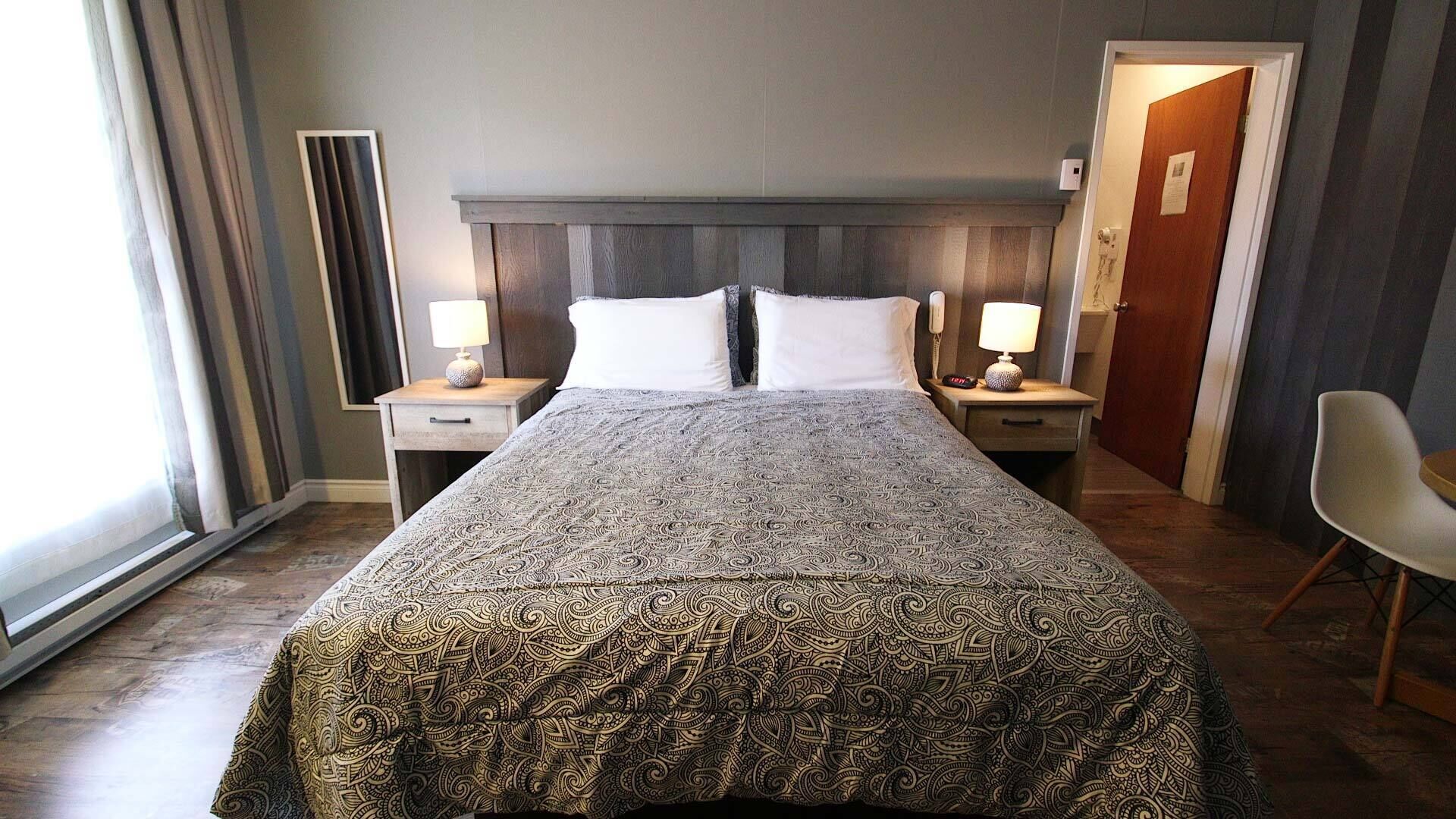 A hotel room with a large bed, two bedside tables with lamps, a chair, and a door.