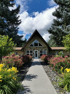 A stone building with a triangular roof, a central entrance, and a pathway leading to it. - Motel La Source (Coaticook)
