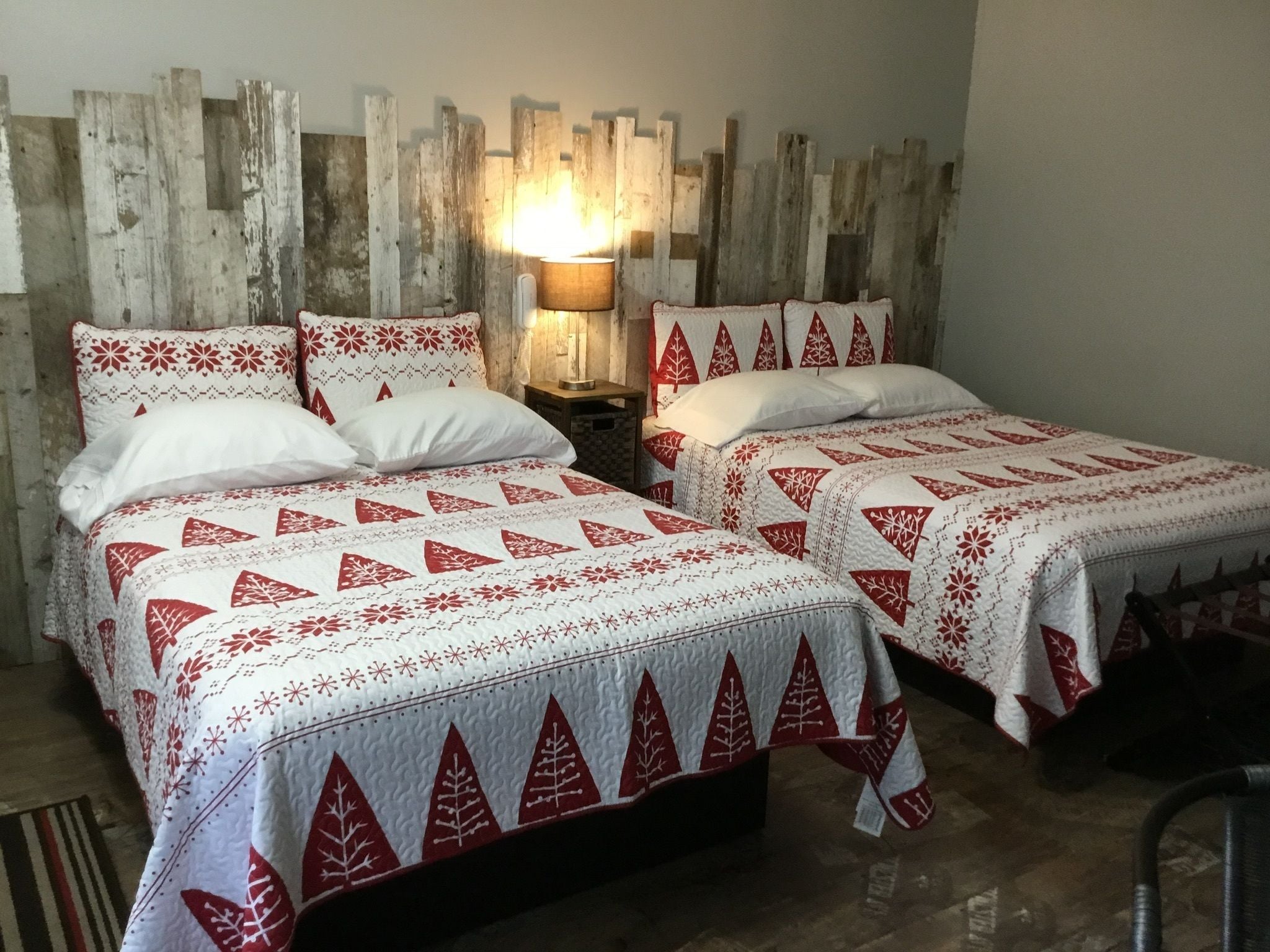 Une chambre avec deux lits, chacun recouvert d’une couvre-lit à motifs rouges et blancs, doté d’une tête de lit en bois et agrémenté d’une table de chevet avec une lampe.