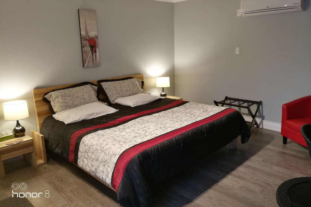 Une chambre bien rangée, avec un lit, des lampes de chevet, une petite table, une chaise et un appareil de climatisation fixé au mur.
