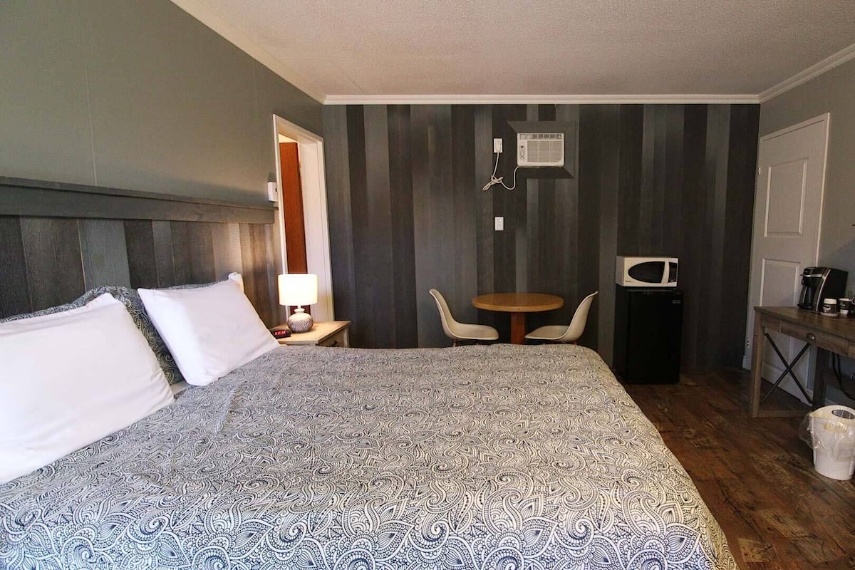 Une chambre d’hôtel avec un grand lit, une petite table avec deux chaises, un four à micro-ondes, une machine à café et un téléviseur fixé au mur.
