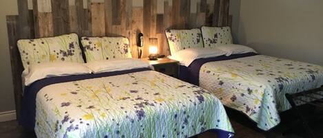A room with two beds, each with floral bedding, a wooden headboard, and a nightstand with a lamp.