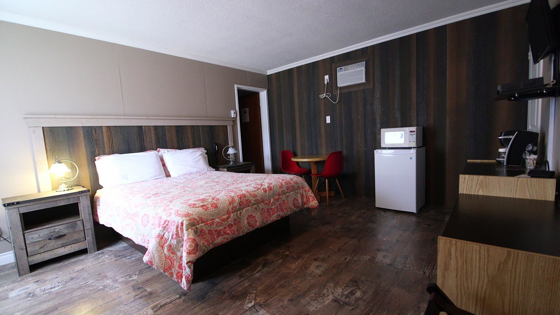 Une chambre d’hôtel comprenant un lit, une table de chevet, une lampe, des chaises rouges, une petite table, un four à micro-ondes et un réfrigérateur.