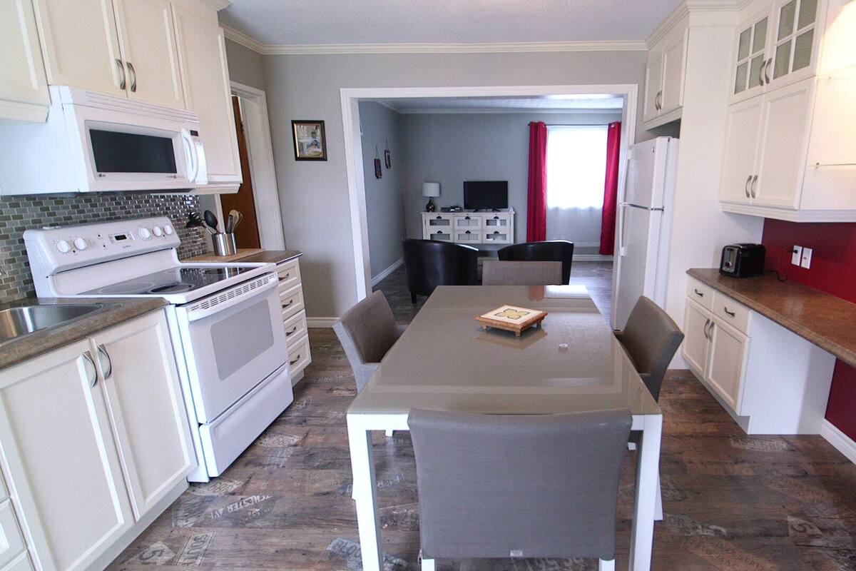 Une cuisine compacte avec des meubles blancs, un four à micro-ondes, une cuisinière et une table à manger avec des chaises.