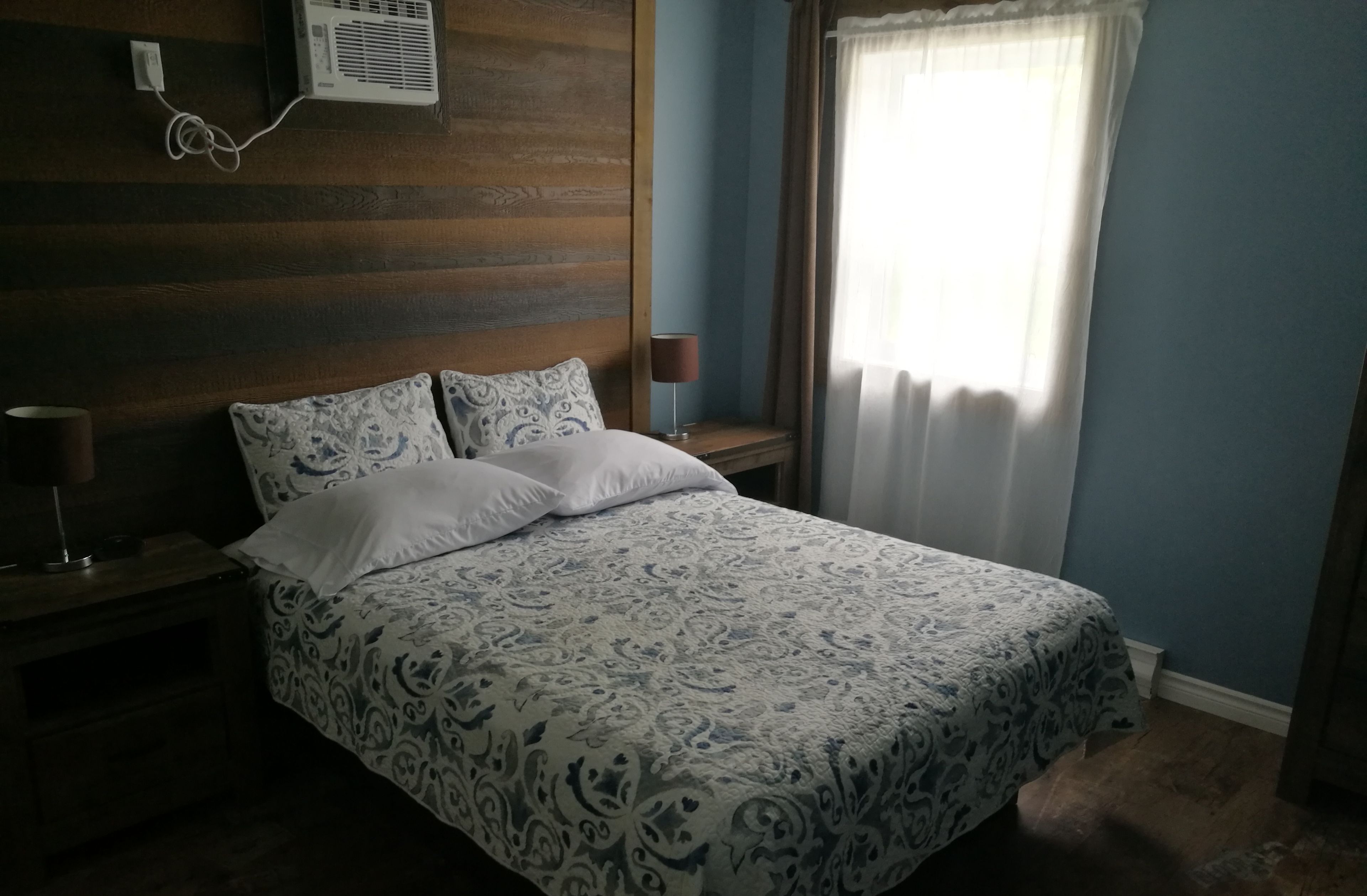 A bedroom with a bed, nightstand, lamp, and an air conditioning unit on the wall.
