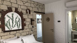 A bedroom with a brick wall, a bed with white bedding, a wooden door, and a bathroom visible through an open door. - Volta Alacati Butik Otel (Cesme)