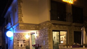 A stone building with a neon sign reading "Volta Alasah Butik Otel". There is a small outdoor seating area with a table and chairs. - Volta Alacati Butik Otel (Cesme)