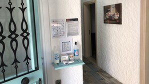 A hallway with a door, a bulletin board with informational posters, a shelf with hygiene products, and a painting on the wall. - Volta Alacati Butik Otel (Cesme)