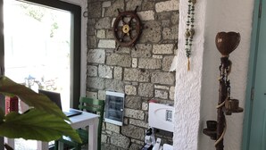 A room with a stone wall, a wooden ship's wheel, a green chair, a table, and a telephone. - Volta Alacati Butik Otel (Cesme)