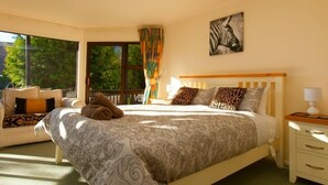 A bedroom with a large bed, a window with curtains, a zebra painting, and a view of trees.