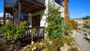 A two-story house with a balcony, a stone pillar, and a garden with various plants and flowers.