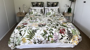 Ein Schlafzimmer mit floralem Bettbezug, zwei passende Kissen, einem Nachttisch mit Lampe und einem gerahmten Bild an der Wand.