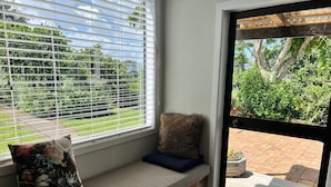 Ein Zimmer mit Fenster zum Garten, eine Bank mit Kissen und eine Tür, die nach draußen führt.