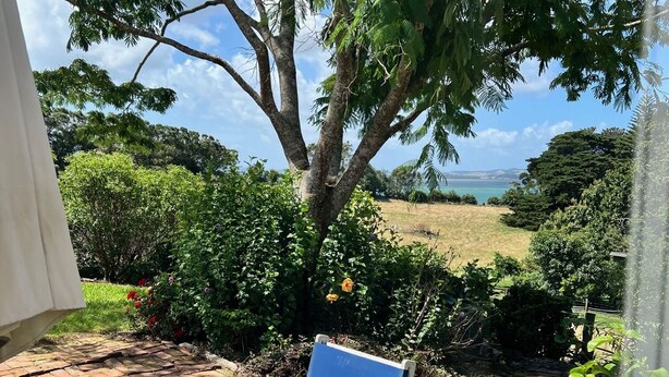 Eine Holzterrasse mit blauem Stuhl und Tisch, umgeben von üppigem Grün und Blick auf das Meer.