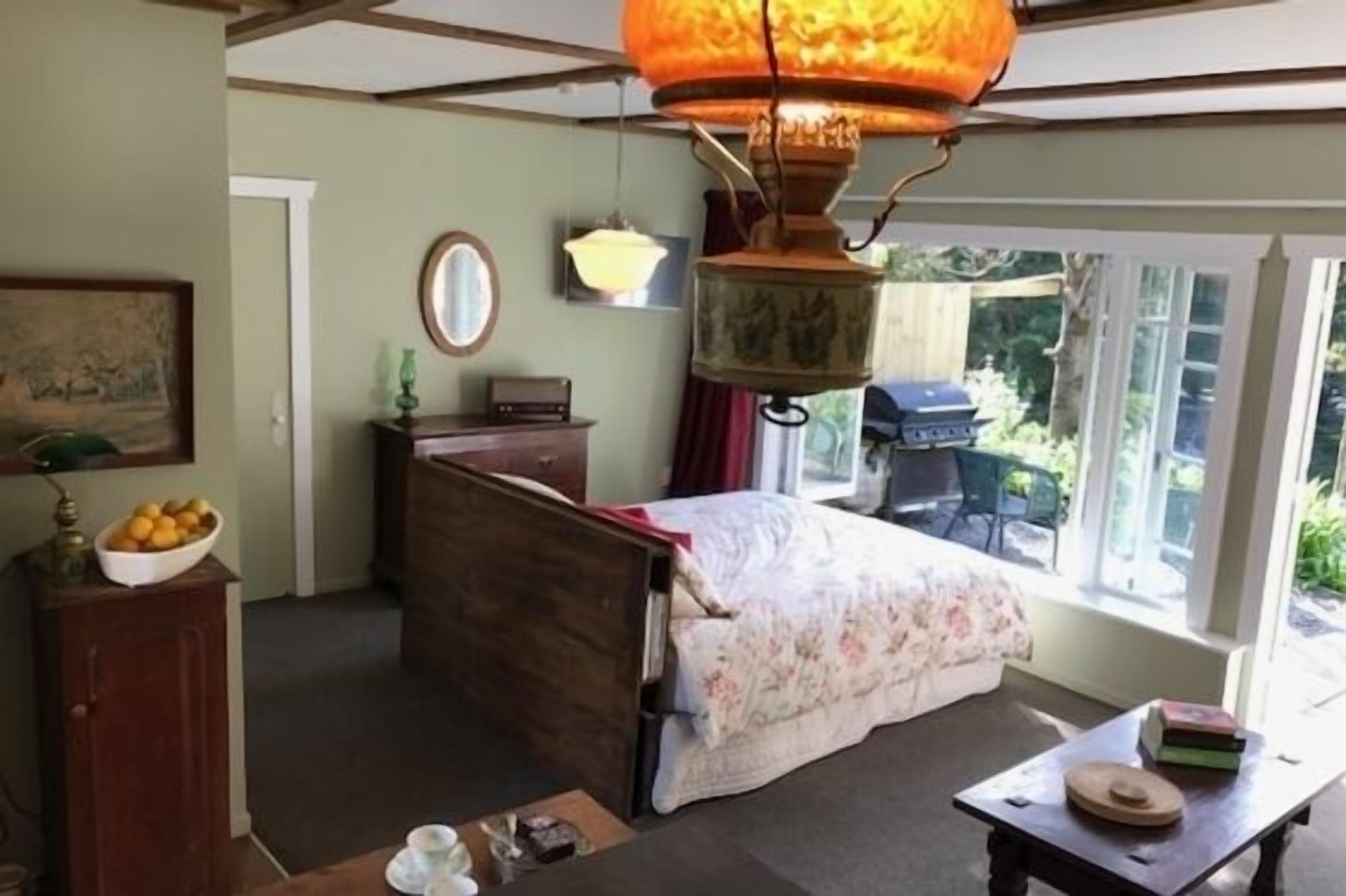 Un dormitorio con cama, mesa, lámpara, ventana y puerta.